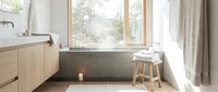 Modern bathroom with concrete soaking tub, wooden vanity, and natural light from large windows, suitable for home design and interior decoration projects.