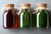 Glass jars with cork stoppers containing red liquid, fresh herbs and green spices on gray background. Natural organic cooking ingredients in rustic style storage.