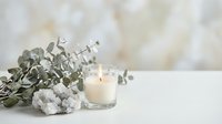 Spa wellness scene with burning candle, eucalyptus branches and white towels on marble surface creating peaceful relaxation atmosphere for self-care.
