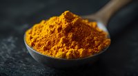 Vibrant orange turmeric powder heaped in metal spoon against dark background, showcasing aromatic Indian spice with rich color and texture for culinary and wellness uses.