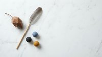 Wooden wand with colorful gemstones and feather on marble surface for spiritual practices, meditation, healing rituals and mystical ceremonies.