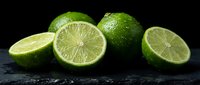 Fresh green limes whole and sliced on dark slate surface showing juicy citrus segments and textured peel for culinary and beverage photography.