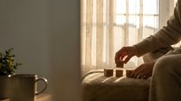 Person relaxing on textured sofa with warm sunlight streaming through window curtains creating peaceful morning atmosphere in cozy living room interior.