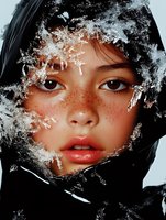 Close up portrait of young Asian woman with freckles wearing black hood, surrounded by delicate snowflakes and frost patterns creating magical winter atmosphere.