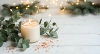 Cozy winter spa scene with burning candle, eucalyptus leaves and pink salt on white wooden background. Holiday relaxation and aromatherapy concept.