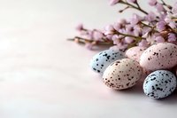 Speckled pastel Easter eggs in pink, blue, and beige tones arranged with delicate pink spring blossoms against soft white background. Seasonal holiday composition.