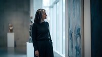 Professional middle-aged woman in black dress standing in modern art gallery looking at abstract paintings, contemplating artwork in contemporary museum space.
