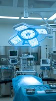 Modern hospital operating room with bright surgical LED light above sterile table, medical monitors and equipment in background.
