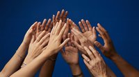 Multiple diverse hands raised up together against blue sky background showing unity teamwork cooperation and community support concept.