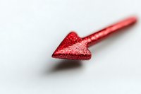 Red glittery arrow pointing left on white background, shallow depth of field creates soft dreamy effect, minimalist composition for love and direction concepts.