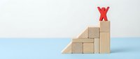 Red figure standing on top of wooden block staircase against blue and white background, representing business growth, success, achievement, and career advancement.