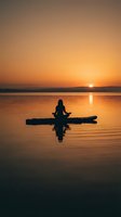 Woman practicing yoga meditation on paddleboard at sunset over calm lake water with golden sky reflection creating peaceful wellness scene.