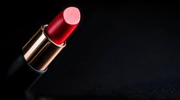 Red lipstick in metallic gold tube on dark background with dramatic lighting and copy space. Professional cosmetic product photography for beauty and makeup advertising.