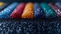 Colorful chalk pastels with glittering water drops on dark background creating artistic macro photography composition. Perfect for creative design projects.