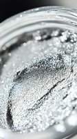 Shimmering silver glitter powder in glass jar, macro view showing sparkly texture for cosmetics, crafting, or holiday decorations.
