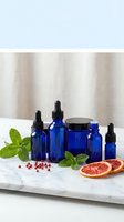 Blue glass essential oil bottles with dropper caps arranged on marble surface with fresh mint leaves, grapefruit slices and pink peppercorns for aromatherapy.