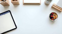 Flat lay workspace with digital tablet, wooden desk organizers, coffee cup, and fresh fruit bowl on white surface for creative projects.