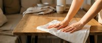 Woman cleaning wooden coffee table with white cloth in modern living room interior for housekeeping and home maintenance tasks.