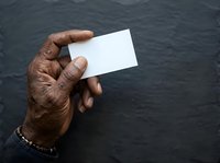 Senior male with dark skin tone holding blank white business card against textured dark background, suitable for corporate branding, identity design, and professional marketing materials.