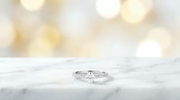 Elegant diamond engagement ring on white marble surface with soft golden bokeh lights background for wedding and jewelry photography.