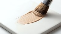 Paintbrush with natural bristles applying beige stroke on white surface, isolated on clean background for design and art projects.