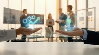 Hands of diverse professionals exchanging glowing digital growth charts and analytics holograms above conference table with team collaborating in modern office background.