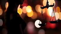 Scales of justice silhouette against blurred bokeh lights background in red and gold tones, symbolizing law, justice and legal proceedings.