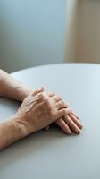 Elderly hands clasped together on white table showing aging skin texture and wrinkles in soft natural light for healthcare and senior lifestyle concepts.