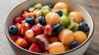 Fresh mixed fruit salad with strawberries, blueberries, cantaloupe, kiwi and grapes in ceramic bowl. Healthy breakfast or snack option for diet nutrition.