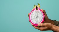 Dragon fruit halved in hand against turquoise background, showcasing white flesh with black seeds. Use for food, nutrition, healthy eating, tropical fruit, wellness, and culinary content.