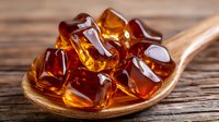 Amber-colored cola cubes on wooden spoon against rustic background, refreshing beverage concept with glossy translucent ice shapes in warm lighting.