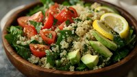 Fresh quinoa salad with avocado, cherry tomatoes and spinach in wooden bowl. Healthy vegetarian meal with lemon garnish for clean eating and nutrition.