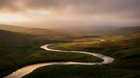 Aerial view of winding river through rolling green hills and moorland landscape during golden hour sunset, suitable for travel and nature backgrounds.
