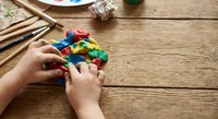 Child hands playing with colorful building blocks on wooden table. Creative learning and development through educational toys and construction play activities.
