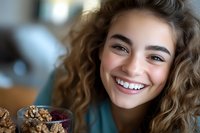 Young woman with curly hair smiling while eating healthy breakfast bowl with granola and berries in modern kitchen setting for wellness lifestyle content.