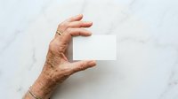 Senior male hand holding blank white business card on marble background, isolated for design mockup and branding presentation purposes.
