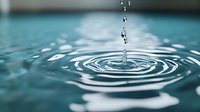 Water drop falling into calm turquoise water creating concentric ripples and splash, captured in macro photography with soft focus background for environmental themes.