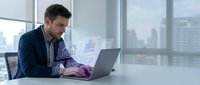 Professional businessman working on laptop with digital analytics charts and graphs in modern office environment with city skyline view.
