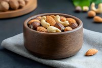 Mixed nuts in wooden bowl on gray cloth napkin for healthy snacking and cooking ingredients.