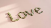 Fresh green pea pods arranged to spell love word on soft pink background with natural shadows, romantic healthy food concept for Valentine's Day celebrations.