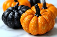 Fresh orange and black decorative pumpkins arranged on white marble surface, creating striking Halloween contrast and seasonal autumn display.