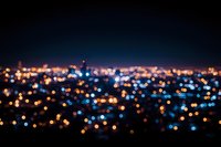 Defocused urban cityscape at night with glowing orange and blue bokeh lights creating magical atmosphere. Blurred panoramic view of metropolitan area.