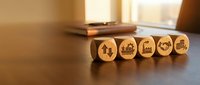 Wooden blocks with industry icons arranged in a row on a desk, representing business growth, manufacturing, and industrial development strategy.