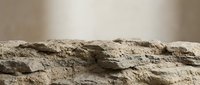 Weathered stone surface with rough textured layers and natural erosion patterns against neutral background for construction and geology projects.