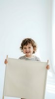 Happy curly-haired toddler boy holding blank beige canvas sign with striped shirt against white background for mockup design and advertising space.