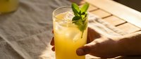 Refreshing yellow citrus cocktail with fresh mint garnish held in hand on sunny outdoor table setting.