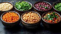 Fresh legumes and herbs in rustic ceramic bowls on dark background - chickpeas, lentils, beans, parsley arranged in row for healthy cooking and protein source.