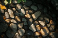 Smooth river stones in natural sunlight creating dramatic shadows and highlights, organic pattern for wellness and spa backgrounds or nature designs.