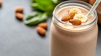 Creamy chocolate banana smoothie with almond milk and nuts in glass jar on dark background, healthy vegan protein drink garnished with fresh ingredients.