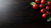 Fresh red cherry tomatoes with green leaves on dark wooden background, corner composition with copy space for text or design elements.